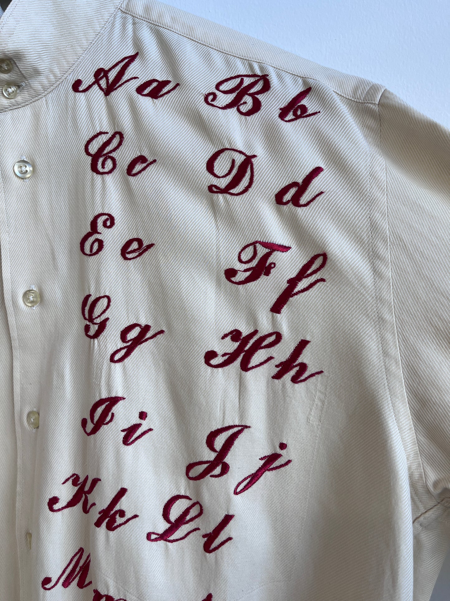 Cursive alphabet sampler on a cream shirt