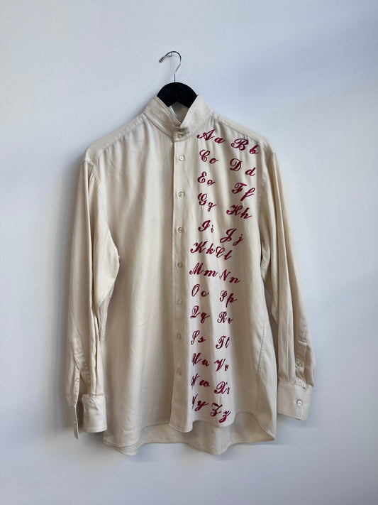 Cursive alphabet sampler on a cream shirt