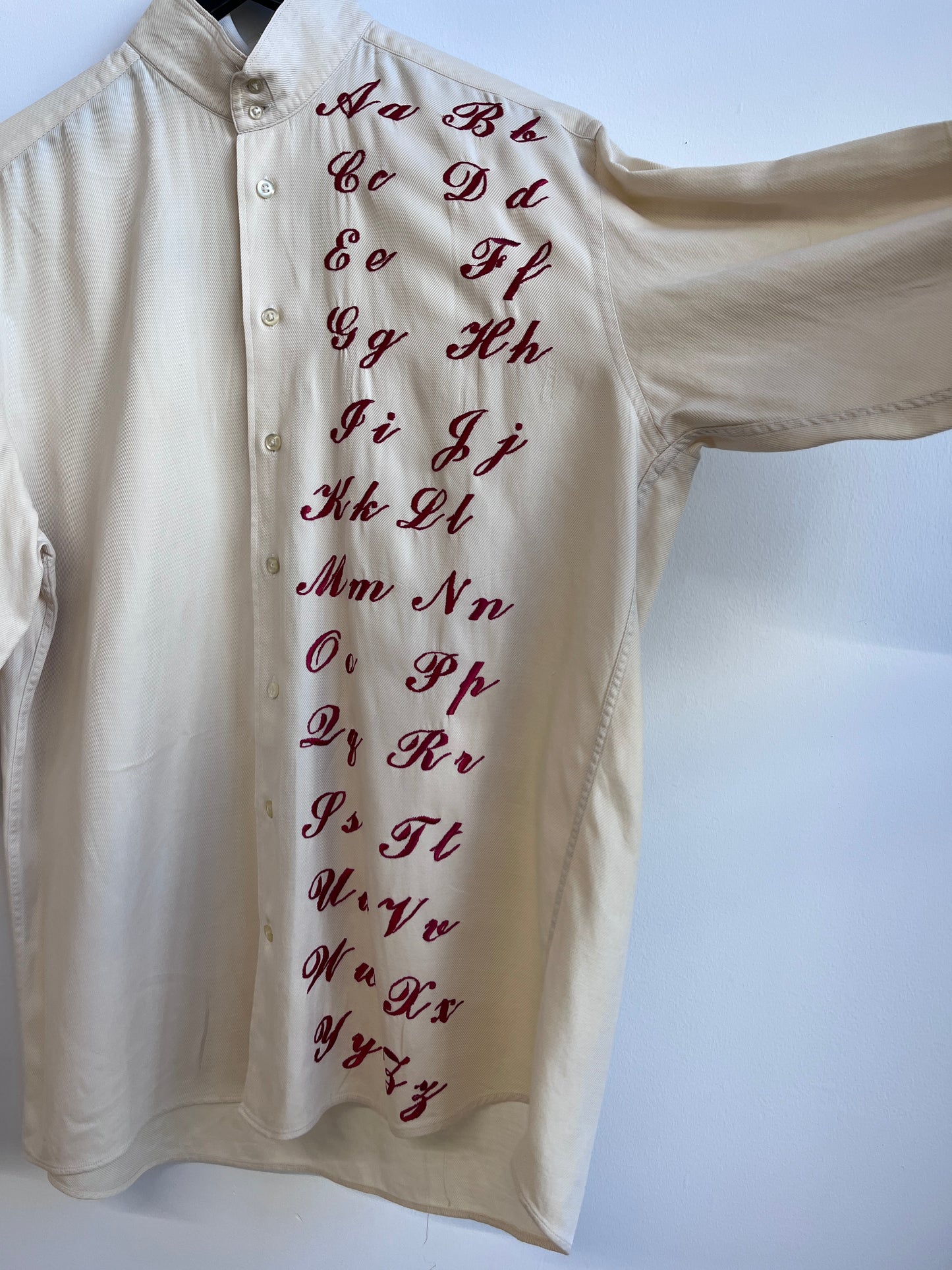 Cursive alphabet sampler on a cream shirt