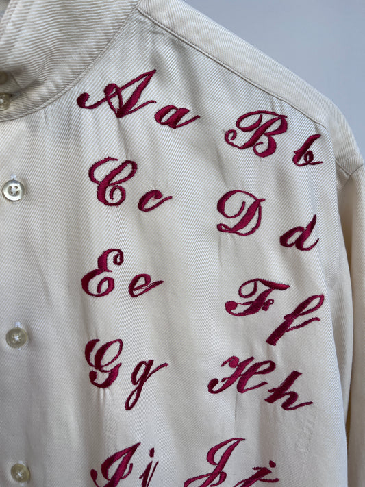 Cursive alphabet sampler on a cream shirt