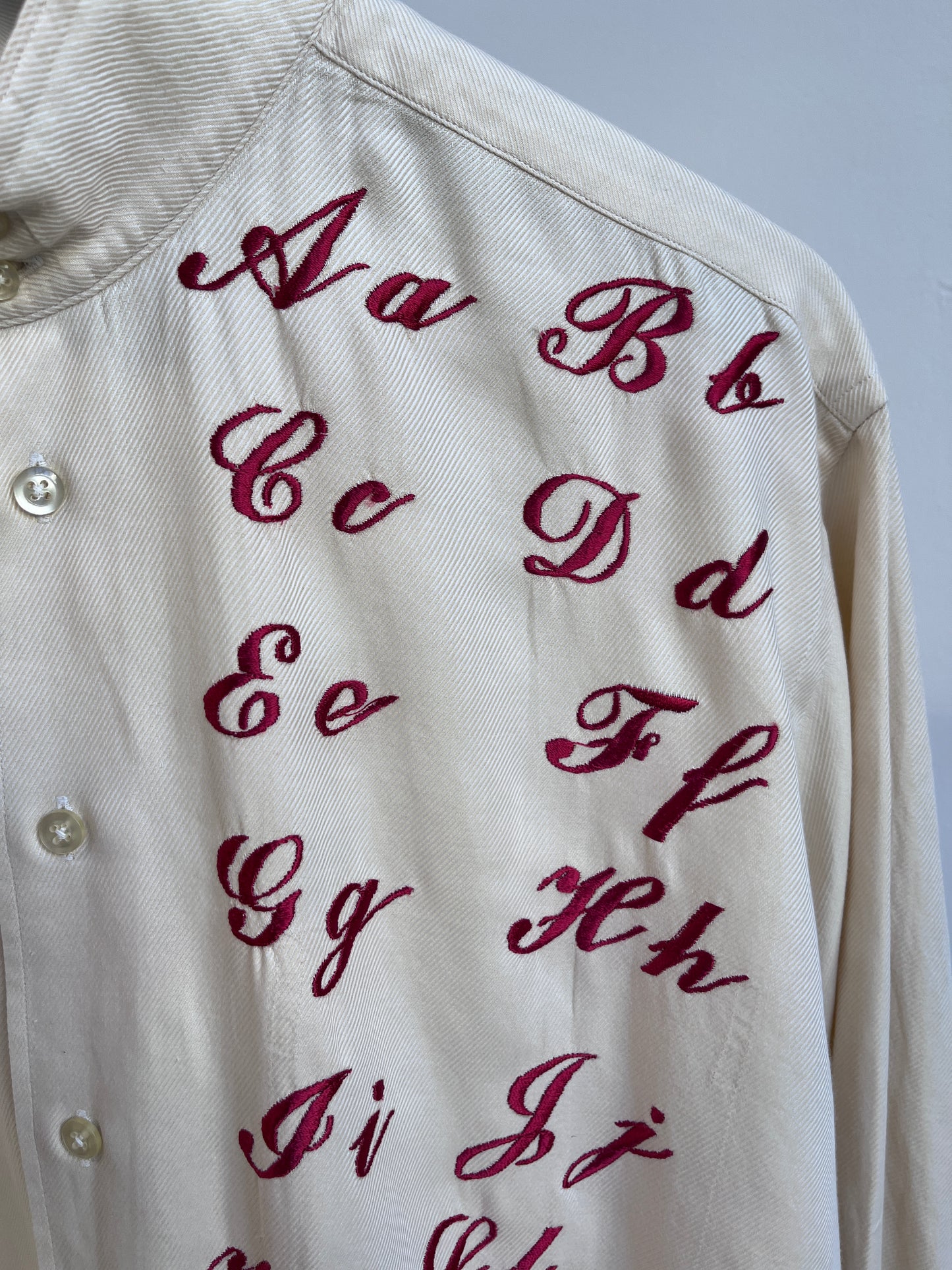 Cursive alphabet sampler on a cream shirt
